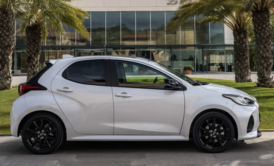 Bijeli gradski automobil sa crnim felgama i detaljima, parkiran ispred moderne zgrade sa palmama u pozadini.