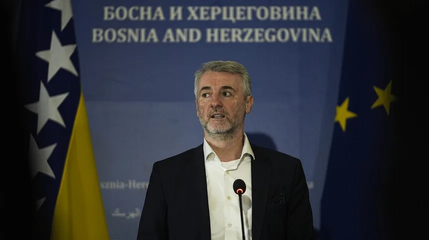 Čovjek u tamnom odijelu i bijeloj košulji govori pred mikrofonom, sa zastavom Bosne i Hercegovine i zastavom Evropske unije u pozadini.