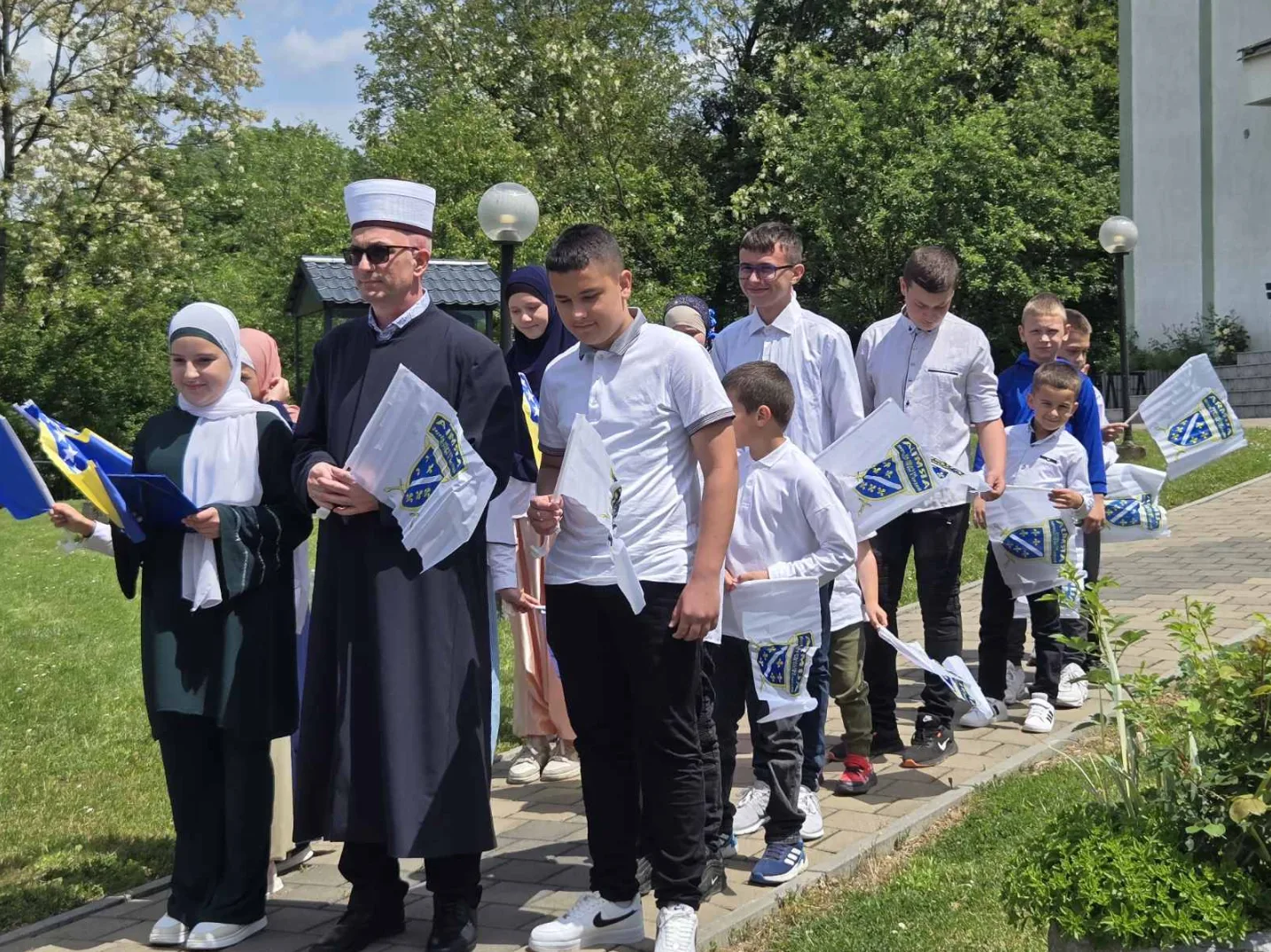 Grupa djece i odraslih sa zastavama Bosne i Hercegovine na otvorenom.