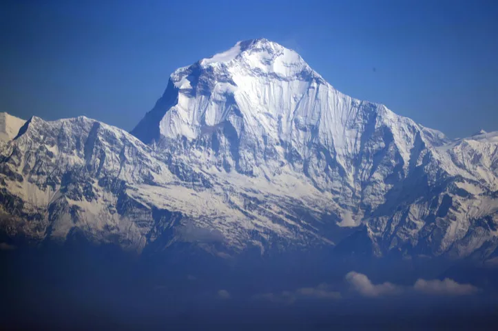 Snijegom prekriveni vrh planine Dhaulagiri pod plavim nebom.