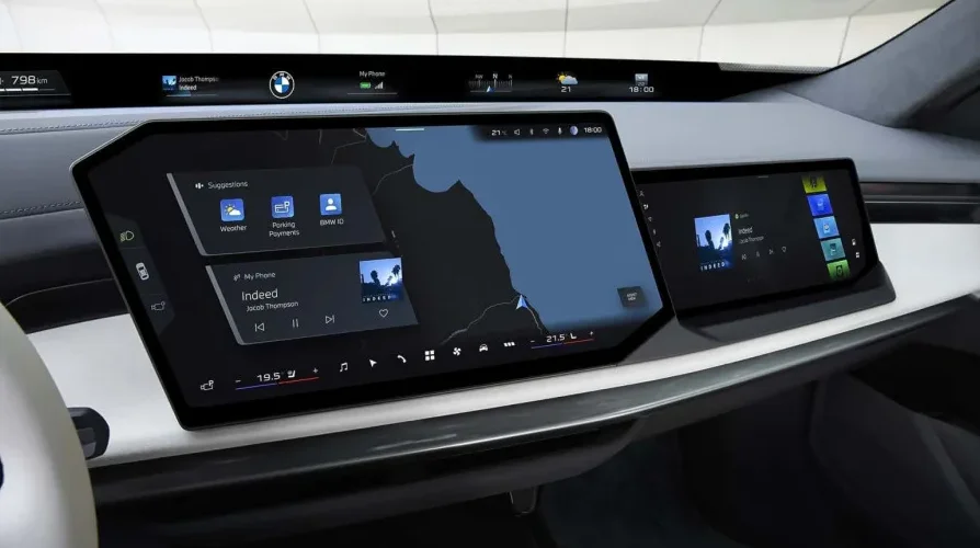 Prikaz modernog digitalnog kokpita automobila sa velikim, zakrivljenim centralnim ekranom na kojem se prikazuje navigacija i opcije poput vremenske prognoze, parking plaćanja i BMW ID.
