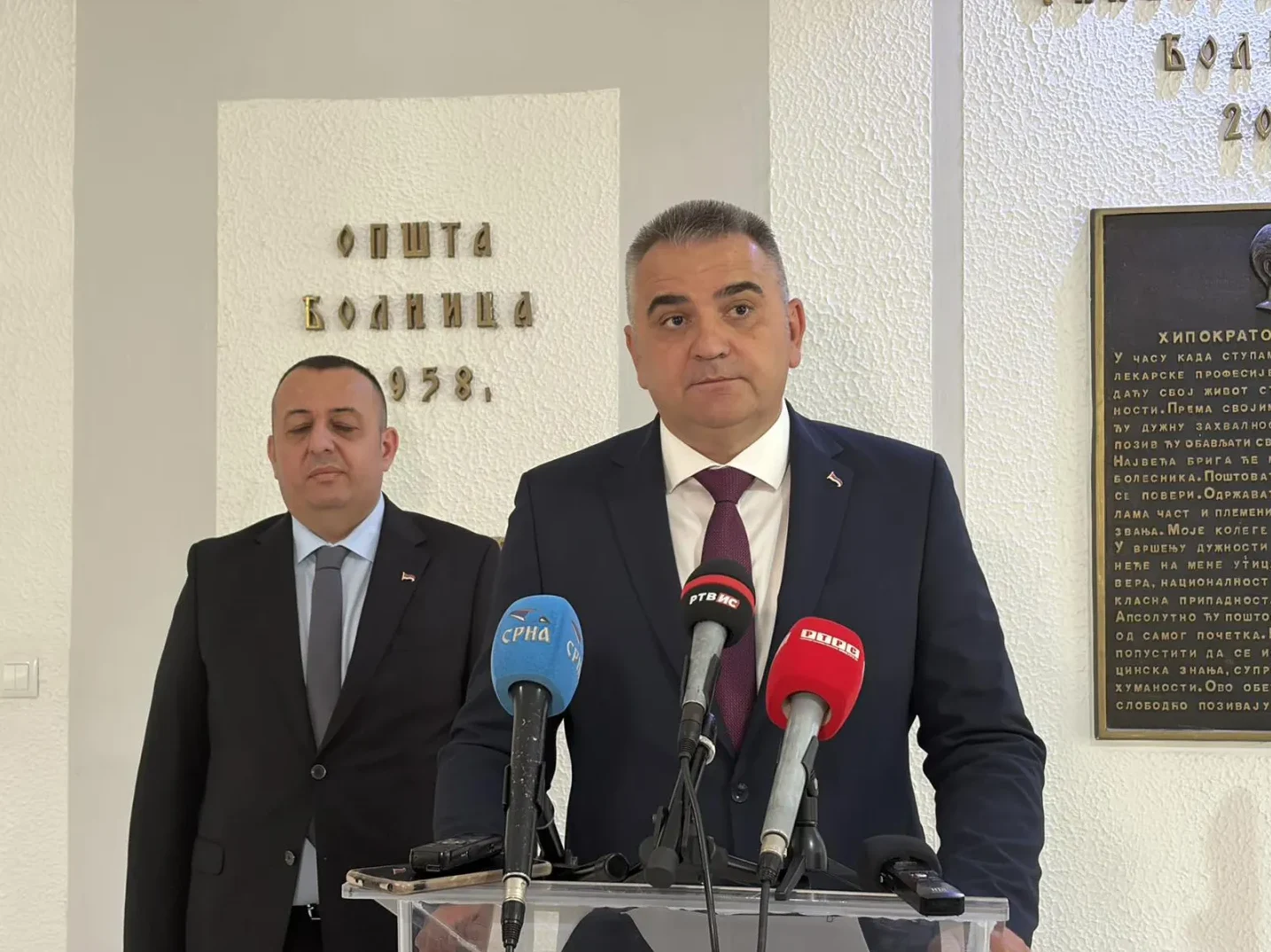 Direktor bolnice i njegov pomoćnik stoje ispred mikrofona na konferenciji za medije.