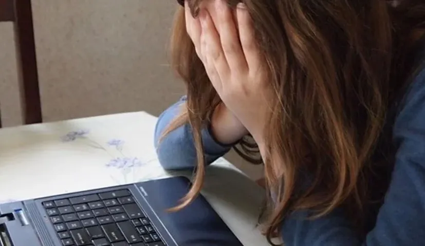 Tužna djevojka pokriva lice rukama ispred laptopa
