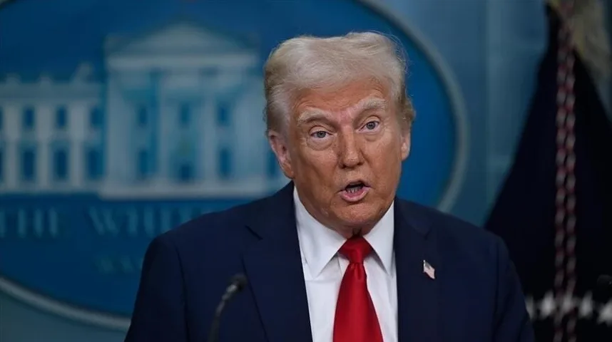 Donald Trump u tamnom odijelu i crvenoj kravati, sa Bijelom kućom u pozadini