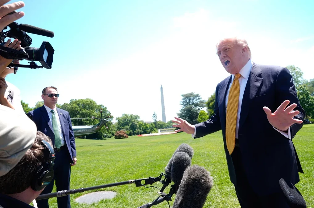 Donald Trump, bivši američki predsjednik, daje izjavu medijima na travnjaku Bijele kuće, s helikopterom u pozadini i Washingtonovim spomenikom u daljini.