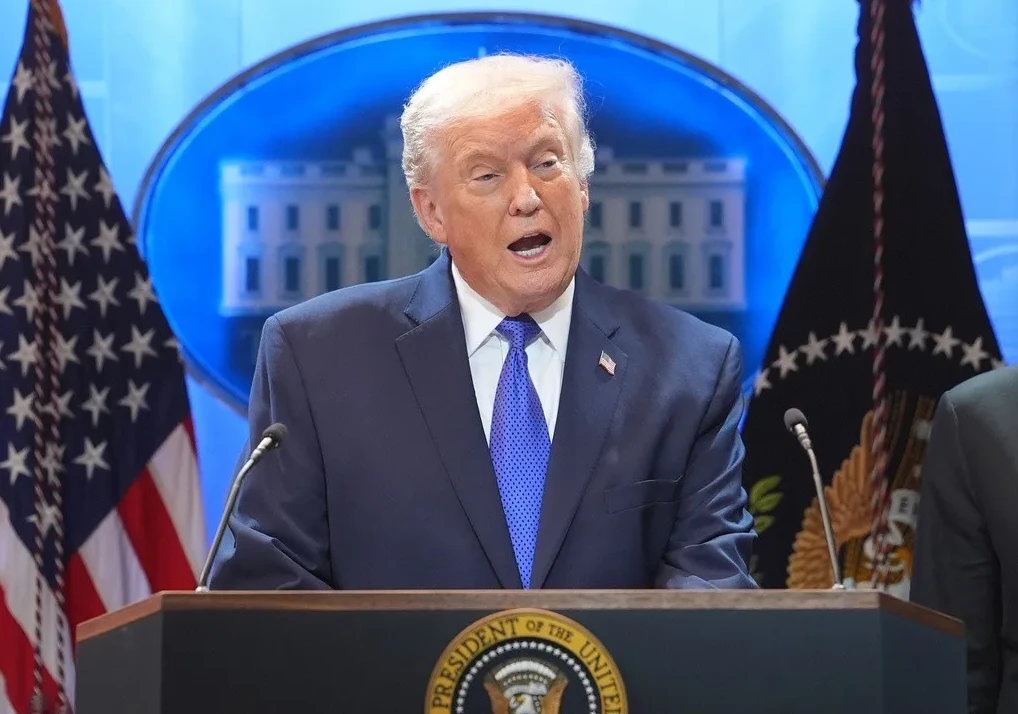 Donald Trump u tamnom odijelu i plavoj kravati govori iza podijuma