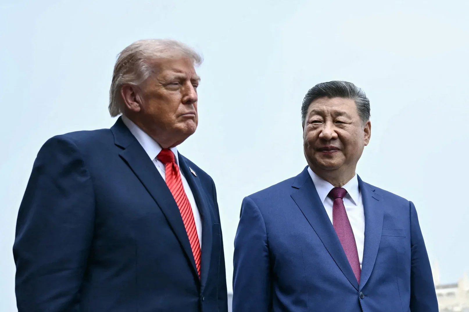 Donald Trump i Xi Jinping u tamnoplavim odijelima i sa crvenim kravatama, gledaju u raznim smjerovima.