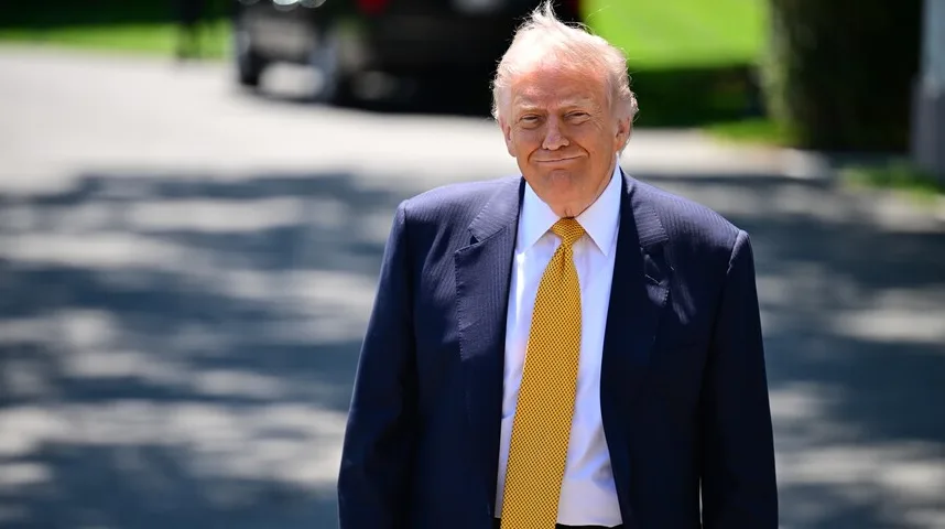 Donald Trump u tamnom odijelu i žutoj kravati, nasmijan, na otvorenom.