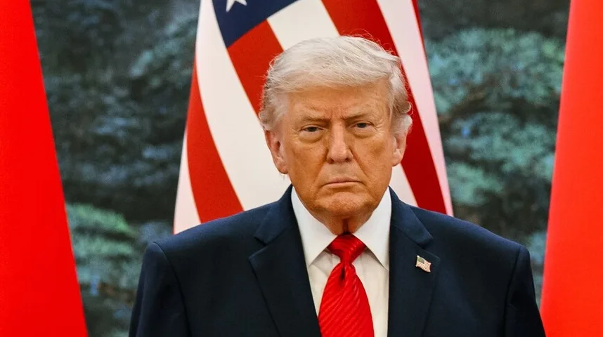 Donald Trump u tamnom odijelu i crvenoj kravati ispred zastave Sjedinjenih Američkih Država.