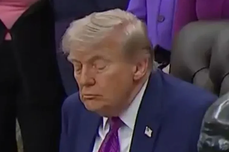 Donald Trump sa zatvorenim očima i opuštenim licem, u plavom odijelu i ljubičastoj kravati.