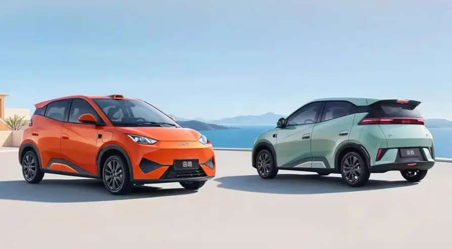 Narandžasti i mentol zeleni električni automobil parkirani jedan pored drugog s pogledom na more i planine u pozadini.