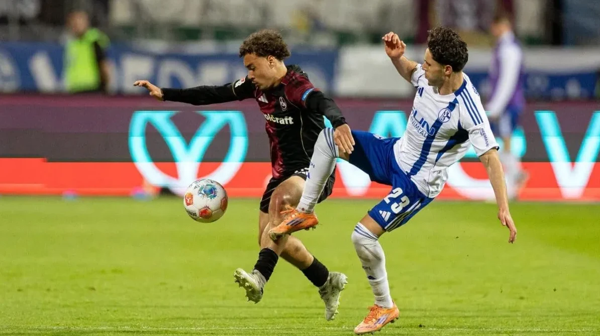 Dva fudbalera u dinamičnom duelu za posjed lopte na zelenom travnjaku fudbalskog terena.