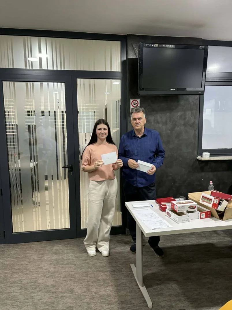 Mlada žena i muškarac drže koverte ispred stola s kutijama poklona.
