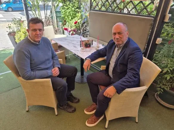 Dva muškarca sjede u udobnim stolicama u bašti kafića.