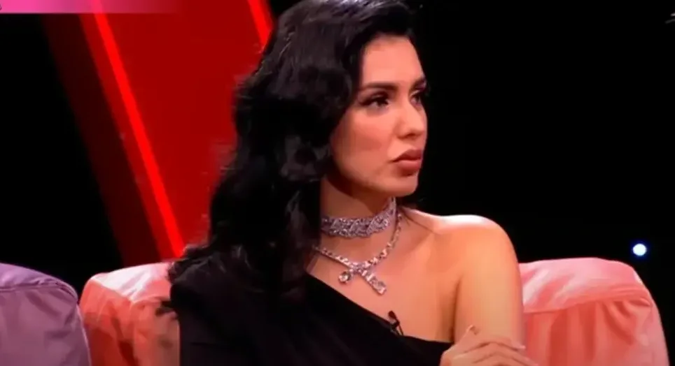 Žena sa crnom kosom i dijamantskim nakitom sjedi u rozoj fotelji
