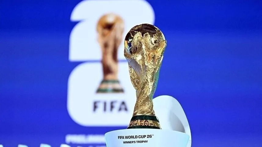 Zlatni trofej FIFA Svjetskog kupa na postolju, sa logom FIFA i natpisom "FIFA WORLD CUP 26" WINNER'S TROPHY". U pozadini se nazire još jedan trofej, zamućen.
