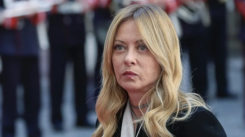 Portret žene s plavom valovitom kosom, sive oči i blago namrgođen izraz lica, nosi crni sako i srebrni nakit oko vrata.
