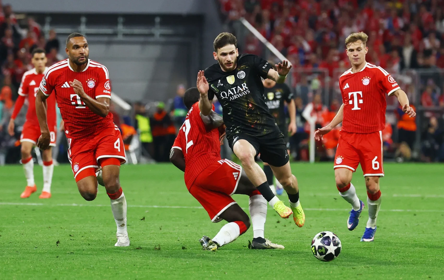 Fudbaleri Bayerna iz Minhena u crvenim dresovima i igrač u crnom dresu Paris Saint-Germaina u akciji na zelenom terenu fudbalskog stadiona.