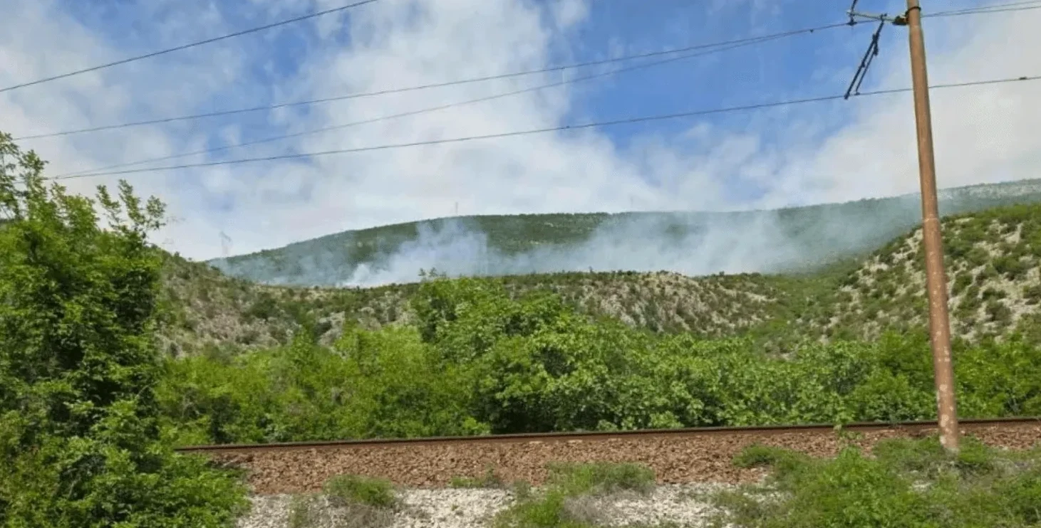 Dim od požara na planinskoj padini iznad željezničke pruge i zelenila.