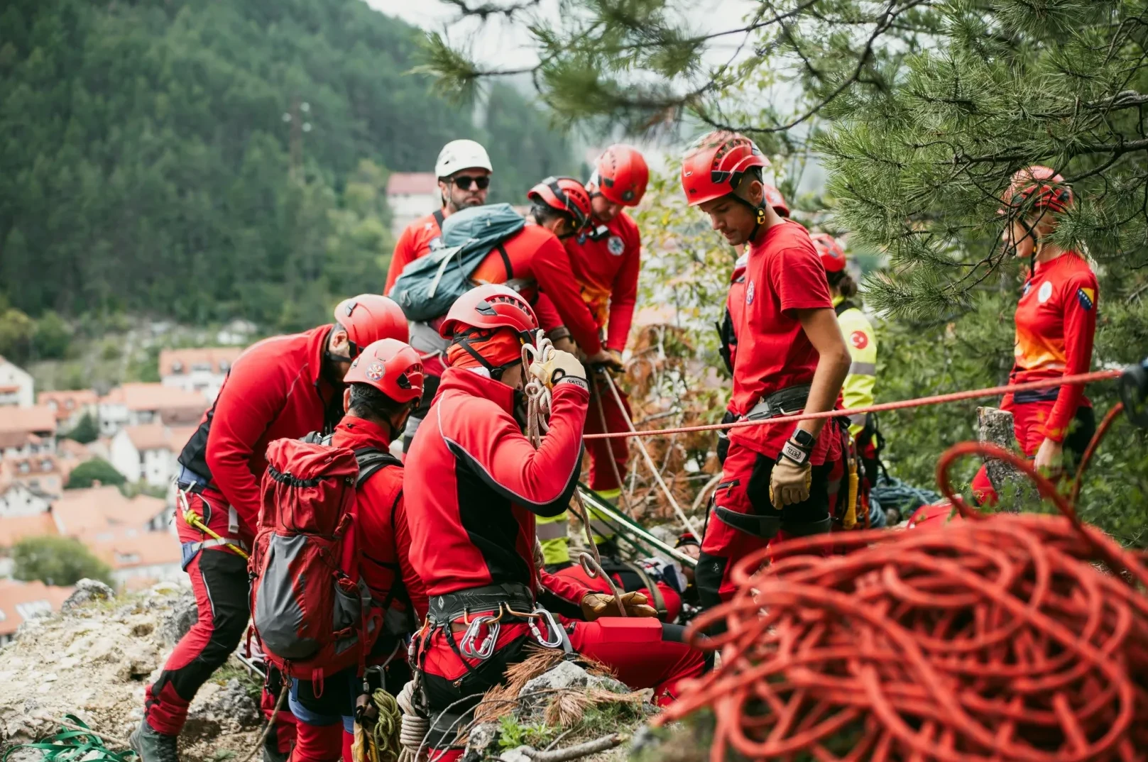 Tim gorske službe spasavanja u crvenim uniformama i kacigama, sa opremom za spašavanje na stijeni, priprema se za akciju.