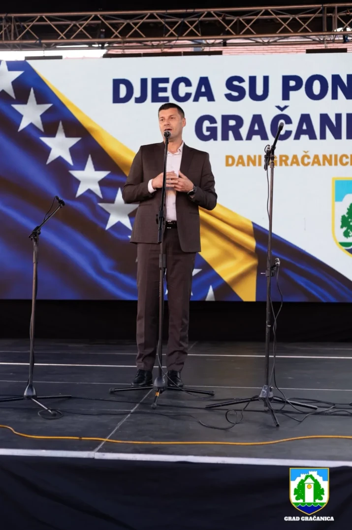 Političar ili javna ličnost obraća se publici sa bine, sa zastavom Bosne i Hercegovine i grbom općine Gračanica u pozadini.