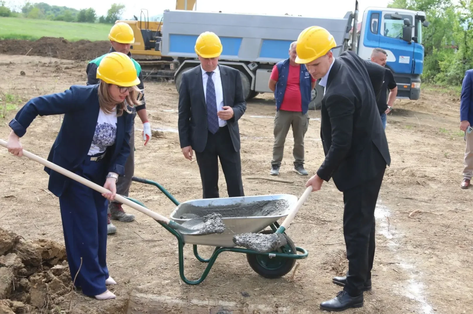 Žena u žutom zaštitnom šljemu i tamnom odijelu lopatom utovara cement u tačke.