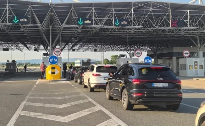 Kolona automobila na graničnom prelazu pod nadstrešnicom sa zelenim strelicama koje pokazuju slobodne trake za automobile.