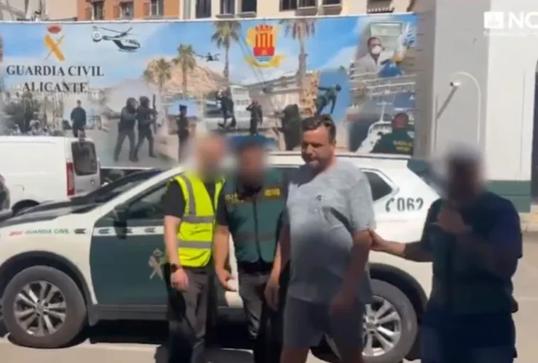 Pripadnici Civilne garde (Guardia Civil) odvode muškarca u blizini službenog vozila u Alicanteu. U pozadini je veliki mural koji prikazuje pripadnike garde i helikopter.