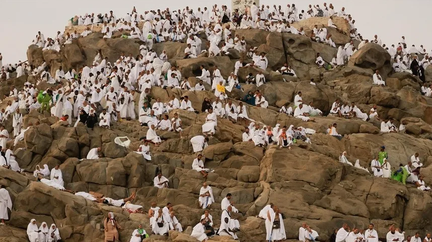 Veliki broj ljudi u bijelim ihramima sjedi i odmara na stjenovitoj planini Arafat.