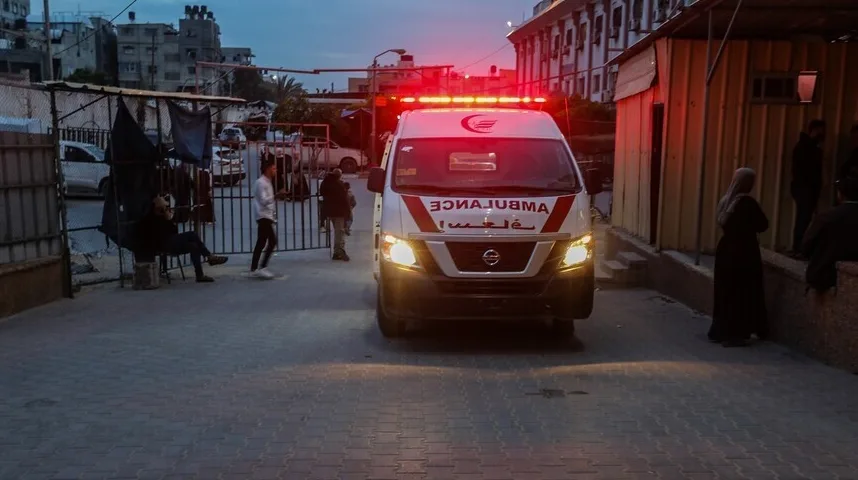 Ambulantno vozilo sa uključenim rotacionim svjetlima parkirano ispred zgrade tokom sumraka.