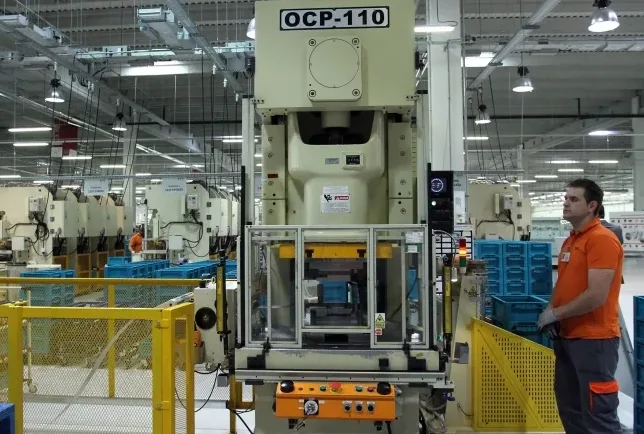 Radnik u narandžastoj uniformi pored industrijske prese OCP-110 u proizvodnom pogonu.