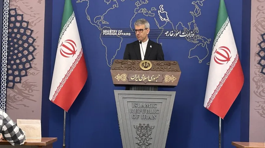 Iranski ministar govora koji stoji iza postolja s iranskim zastavama i kartom svijeta u pozadini.