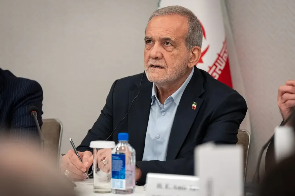 Iranski zvaničnik sa srebrnom kosom i bradom sjedi za stolom i govori, noseći tamnoplavo odijelo i svijetlo plavu košulju. Na njegovom lijevom reveru primjetan je mali bedž sa zastavom.