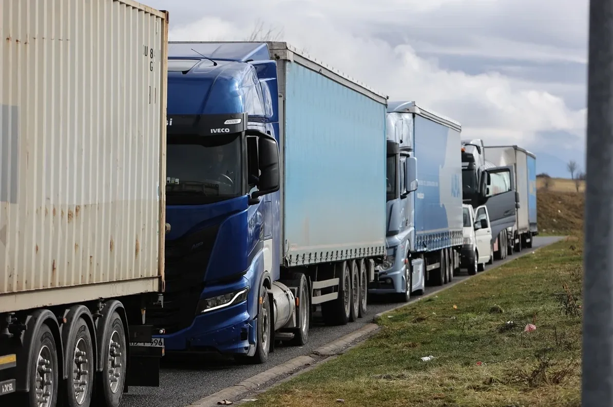 Kolona kamiona plave i bijele boje parkirana na putu pored zelene površine, s natpisom "IVECO" na jednom od kamiona.