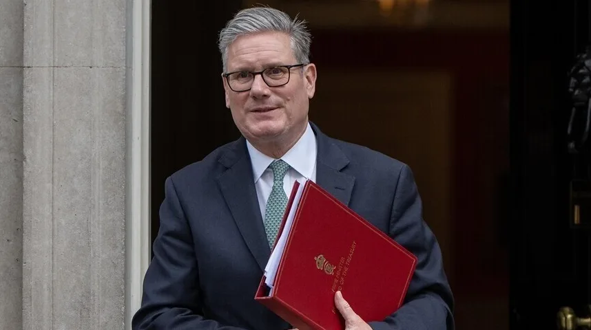 Britanski političar Keir Starmer nosi tamno odijelo i zelenu kravatu, te drži crvenu fasciklu s natpisom "Prime Minister"