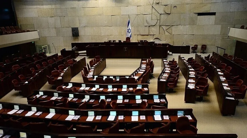 Prazna sala Kneseta, sjedište izraelskog parlamenta, sa tamnosmeđim sjedištima raspoređenim u polukrug i zastavom Izraela na podijumu.