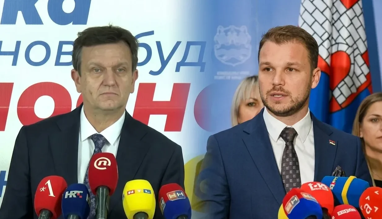 Dva muškarca u odijelima stoje pred brojnim mikrofonima medija, a iza njih se nalaze zastave i natpisi.