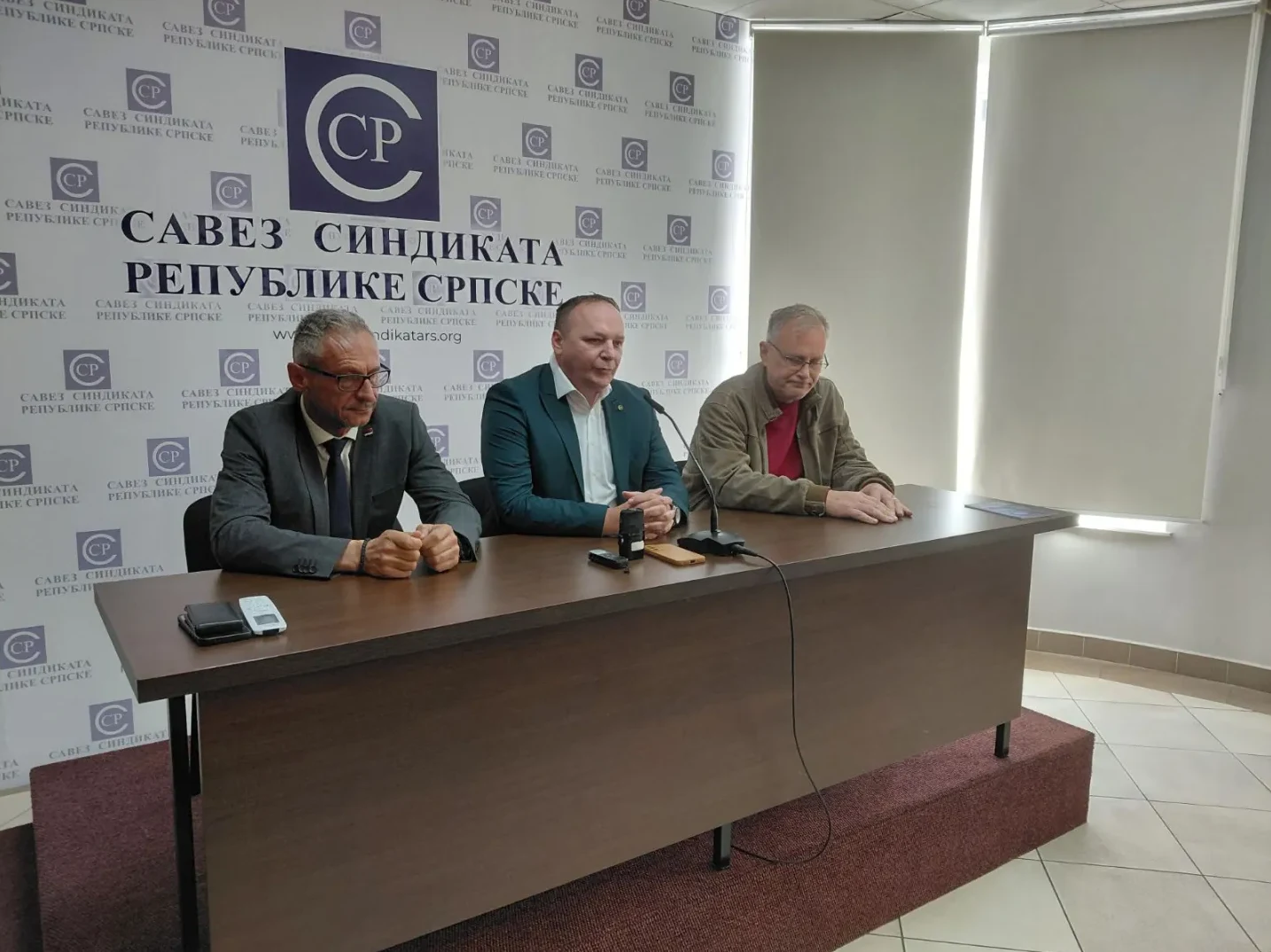 Tri muškarca sjede za stolom ispred banera sa logom Saveza sindikata Republike Srpske.