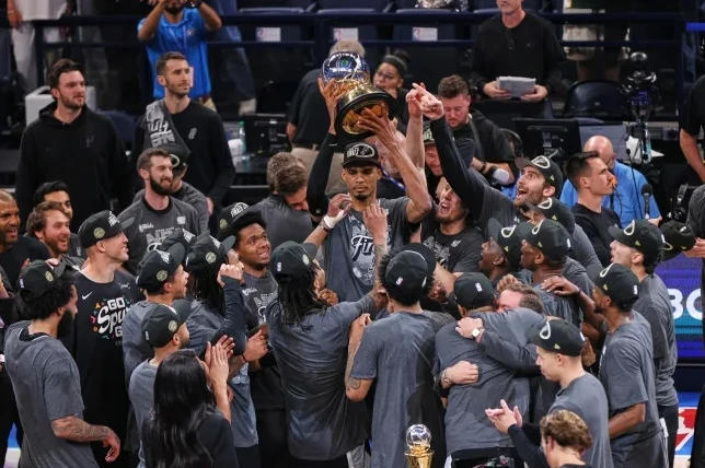 Košarkaški tim San Antonio Spurs podiže trofej NBA lige u zrak, okruženi saigračima i navijačima.