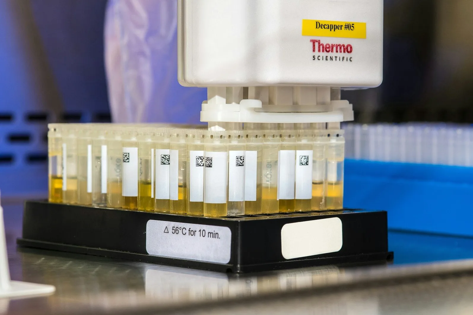 Laboratorijske epruvete ispunjene žutom tečnošću, poređane u crnom držaču, sa automatskim uređajem iznad.