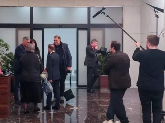 Grupa ljudi okupljena u holu, dok ih snima filmska ekipa sa kamerom i mikrofonom.