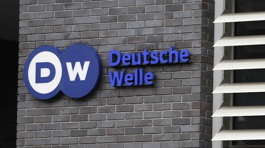 Logo "DW" i natpis "Deutsche Welle" ispisani plavim slovima na tamnosivoj ciglenoj fasadi.