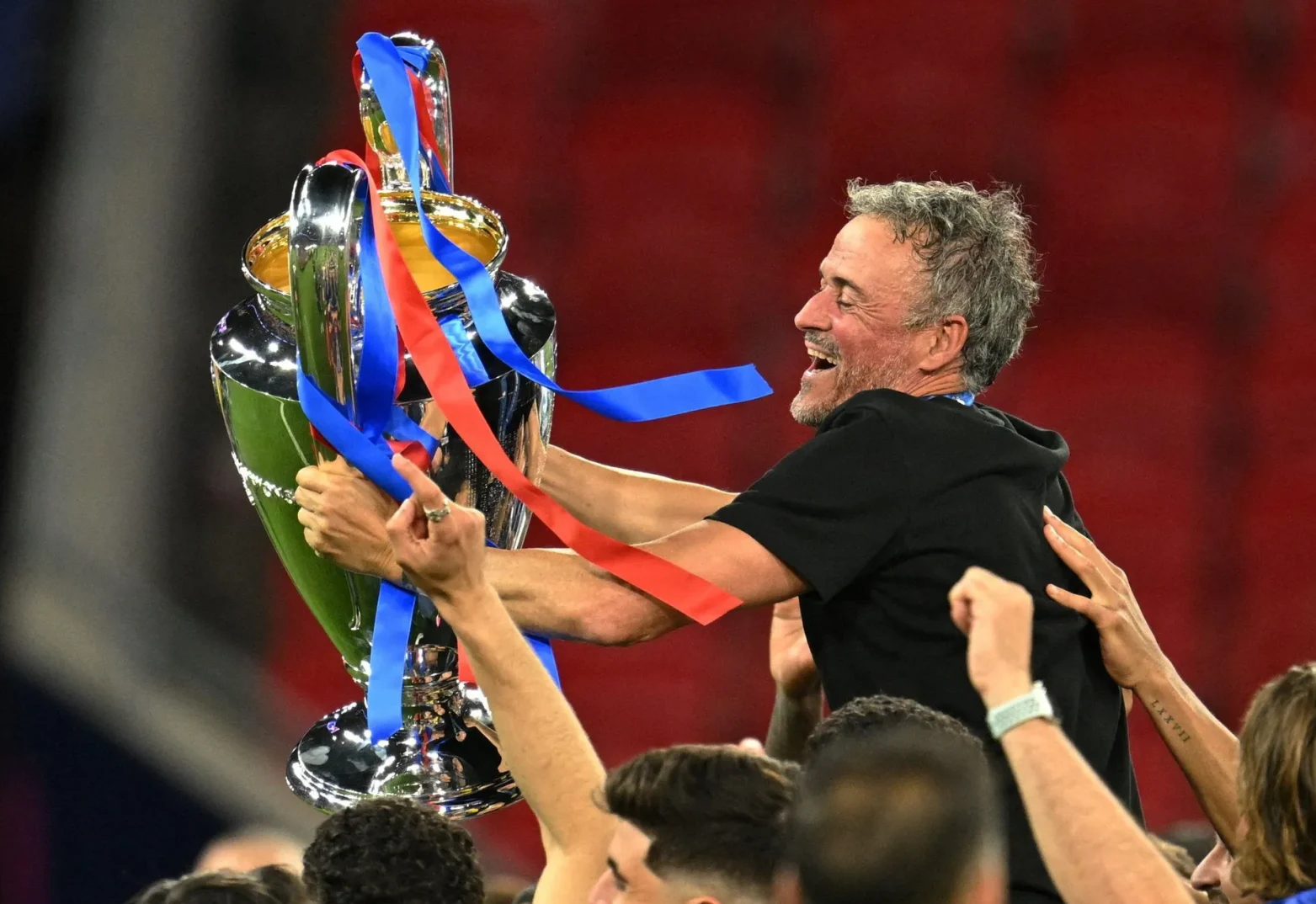 Fudbalski trener Luis Enrique drži podignut pehar Lige šampiona, dok ga slave njegovi igrači.