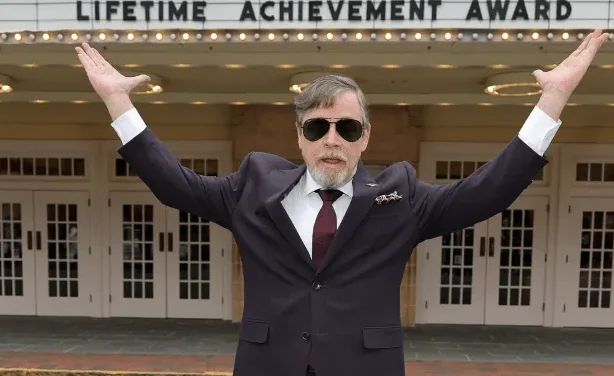 Mark Hamill podiže ruke u znak pozdrava ispred zgrade sa natpisom "Lifetime Achievement Award"