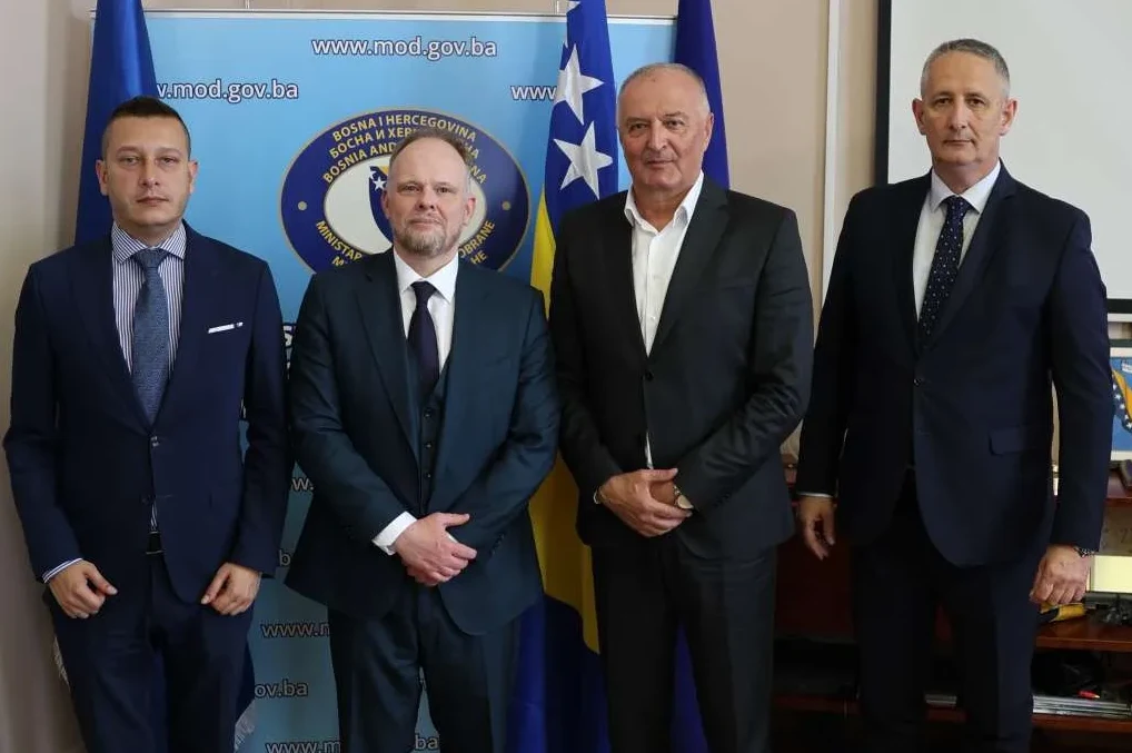 Četiri muškarca u odijelima poziraju ispred zastave Bosne i Hercegovine.