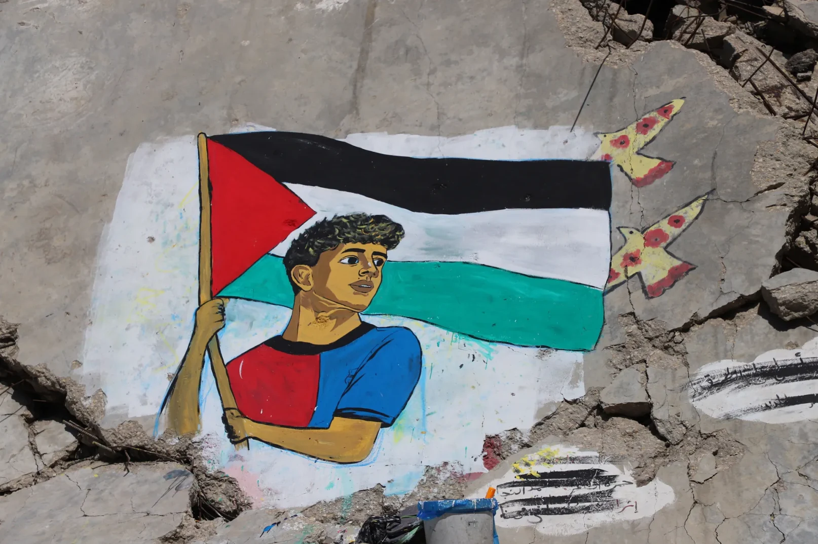 Grafiti na zidovima prikazuje mladog Palestinca koji ponosno drži palestinsku zastavu, a iznad njih lete ptice kao simbol nade i slobode.