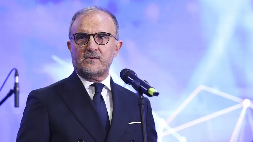 Ozbiljan muškarac u tamnom odijelu i sa naočarima govori za mikrofonom na bini.