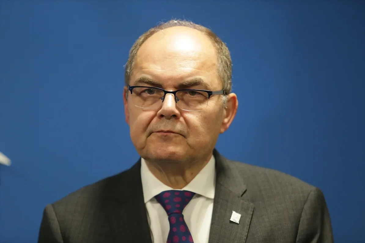 Portret muškarca srednjih godina koji nosi naočale, tamno odijelo i ljubičastu kravatu sa šarama.