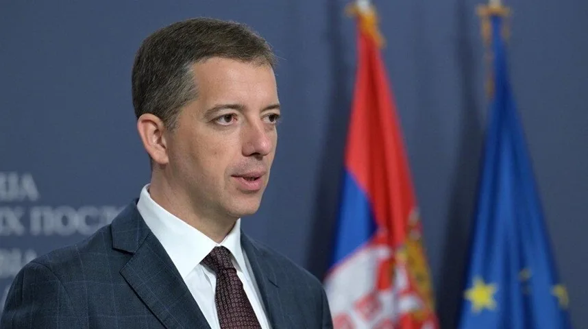 Portret muškarca u tamnom odijelu i bijeloj košulji sa tamnom kravatom, koji stoji ispred zastave Srbije i Evropske unije.