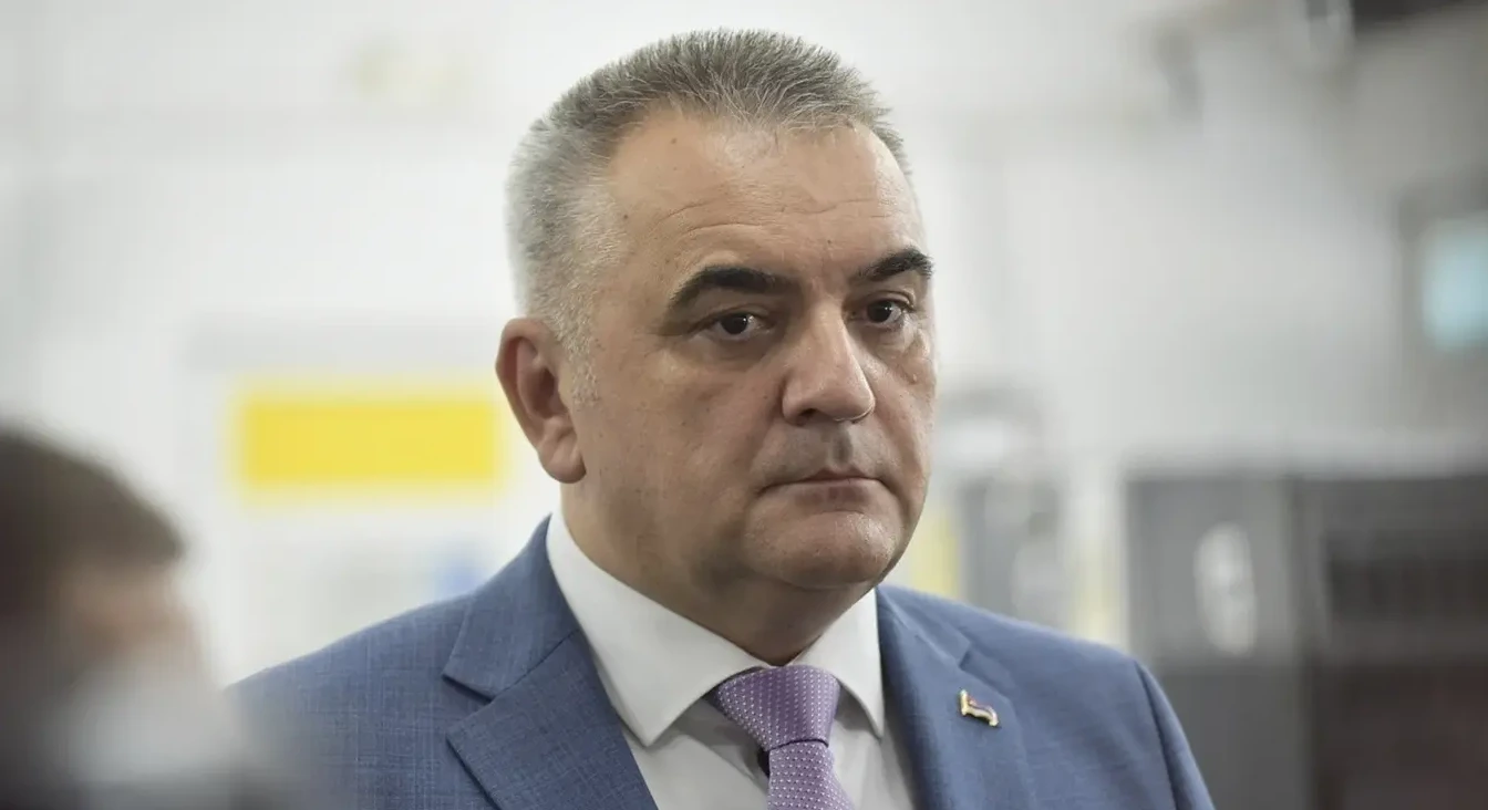 Portret muškarca srednje dobi sa sijedom kosom, obučenog u plavi karirani sako i bijelu košulju sa ljubičastom kravatom sa šarama.